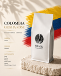A white coffee bag labeled 'COLOMBIA GEISHA ROSE' and 'CRACK COFFEE ROASTRY' stands on a textured stone slab against a cream background with bold yellow, blue, and red brushstroke graphics and shadow overlays.