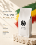 A white bag of Crack Coffee Roastery Ethiopia Anaerobic coffee stands on a textured stone slab against a warm beige background with green, yellow, and red brushstroke accents and product text on the left.